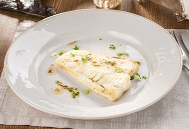 Un pescado cocinado al vapor en un plato blanco.