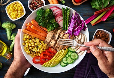 Plato con zanahoria, maíz, brócoli y espárragos cocinados al vapor, junto a otros alimentos.